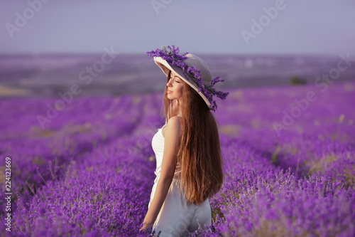 Beautiful healthy long hair. Back view of Young teen girl in hat over lavender field. Happy carefree woman with shiny hairstyle enjoying sunset. Outdoors portrait. Provence, France.