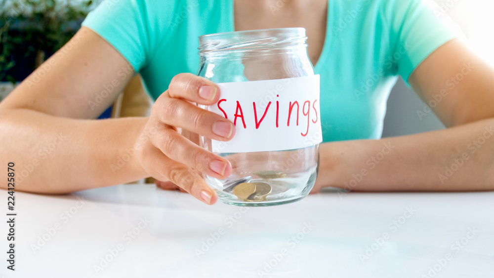 Closeup image of young woman holding glass jar with few coins in it