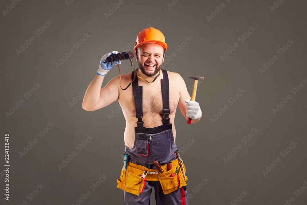 Funny fat bearded repairman with binoculars on a gray background.