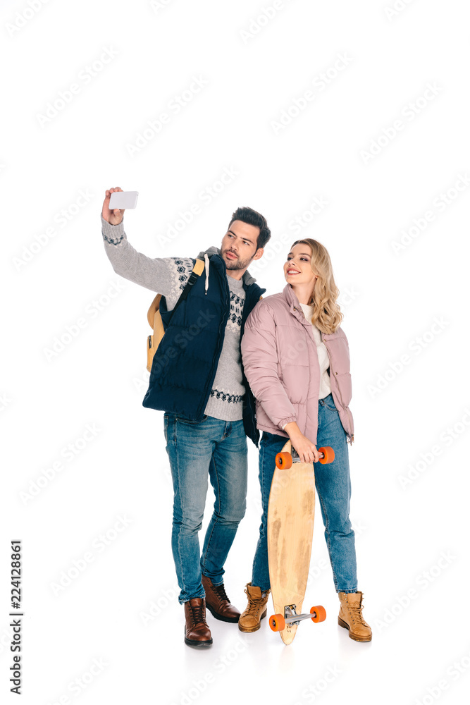 Obraz premium smiling young couple with backpack and skateboard taking selfie with smartphone isolated on white