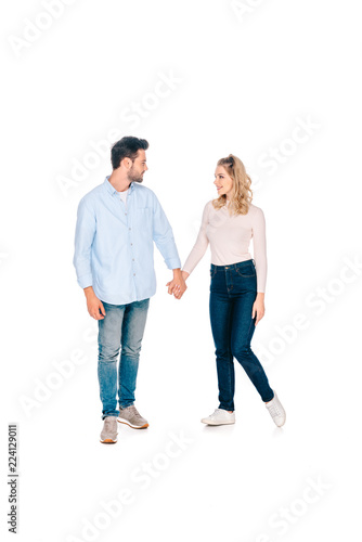 full length view of happy young couple holding hands and smiling each other isolated on white