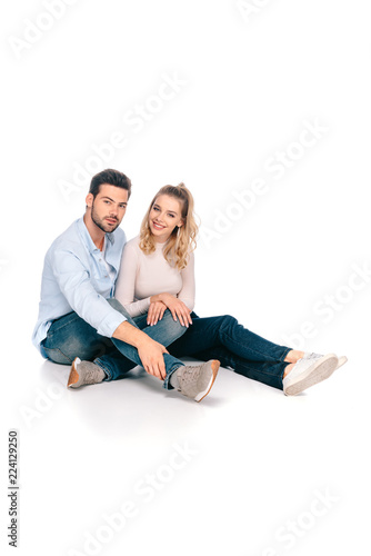 happy young couple sitting together and smiling at camera isolated on white