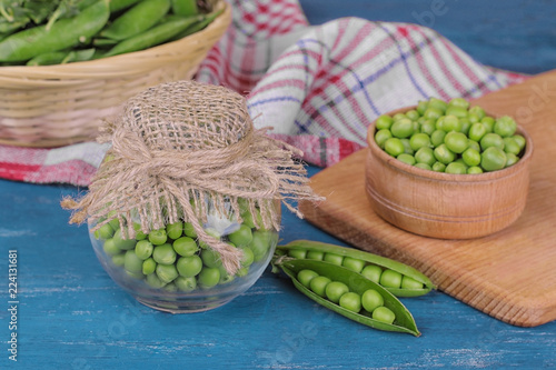 Green peas in a jar with fresh peas on a blue wooden table
