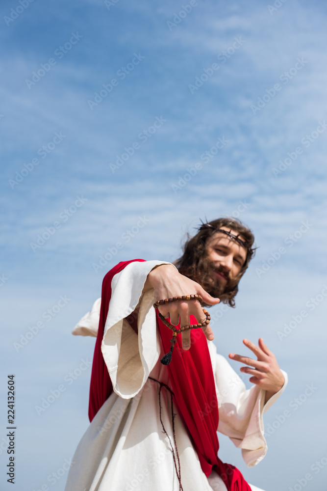 Fototapeta premium low angle view of Jesus having fun and showing two fingers with rosary against blue sky