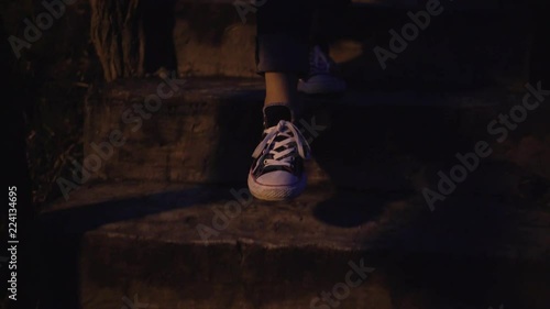 Silhouette of girl legs in sneakers walking downstairs at night in moonlight.