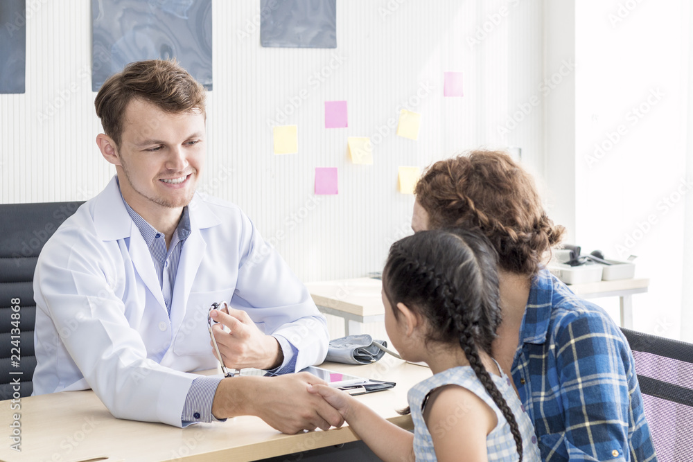 Fototapeta premium Pediatrician (doctor) man examining child with stethoscope at surgery .Mother Caucasian and kid smiling in hospital room.Copy space.