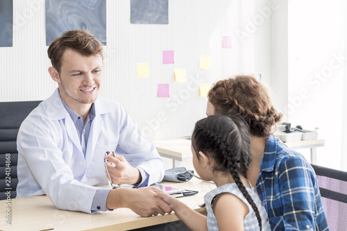 Pediatrician (doctor) man examining child with stethoscope at surgery .Mother Caucasian and kid smiling in hospital room.Copy space.
