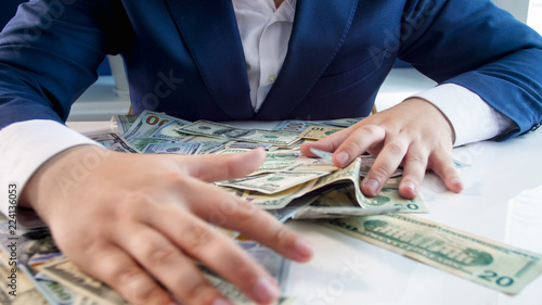 Closeup photo of greedy businessman grabbing money lying on office desk