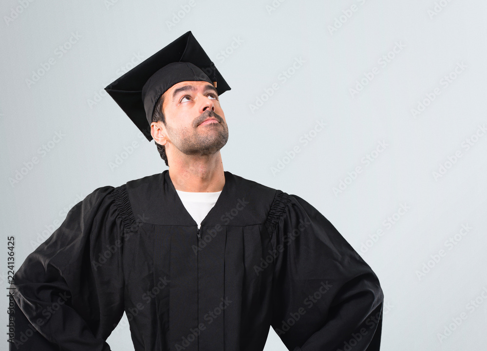 Man on his graduation day University stand and looking up on grey background Man on his graduation day University stand and looking up on grey background
