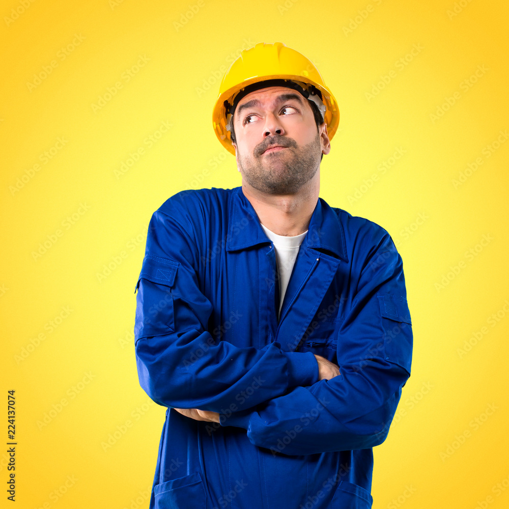 Young workman with helmet making unimportant and doubts gesture while lifting the shoulders on yellow background Young workman with helmet making unimportant and doubts gesture while lifting the shoulders on yellow background