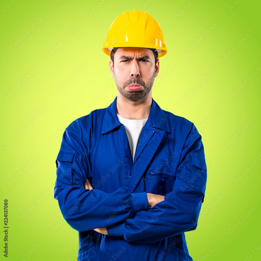 Young workman with helmet with sad and depressed expression. Serious gesture on green background Young workman with helmet with sad and depressed expression. Serious gesture on green background