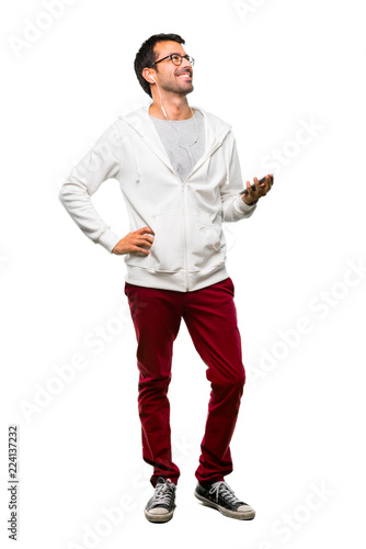 A full-length shot of a Man with glasses and listening music posing with arms at hip and laughing on white background