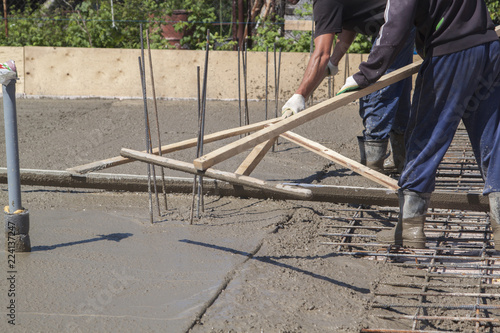 two workers leveling fresh concrete slab with a special wooden working tool