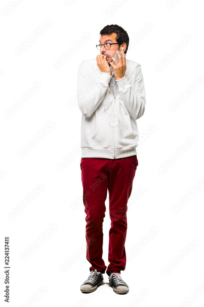 A full-length shot of a Man with glasses and listening music is a little bit nervous and scared putting hands to mouth on white background A full-length shot of a Man with glasses and listening music is a little bit nervous and scared putting hands to mouth on white background