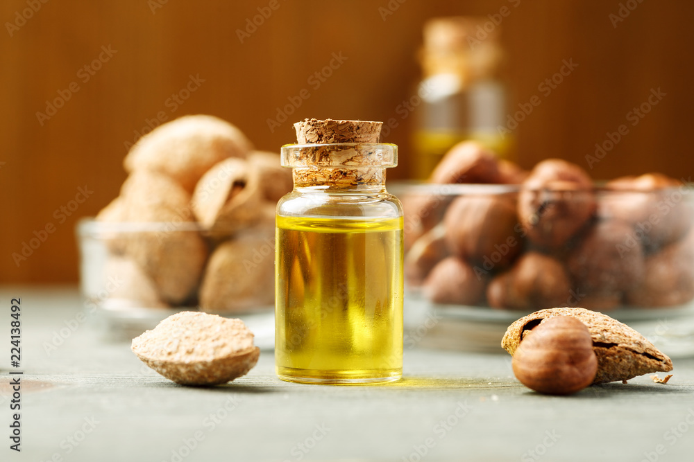 Small glass vial with wooden cork and different nuts in the background Small glass vial with wooden cork and different nuts in the background