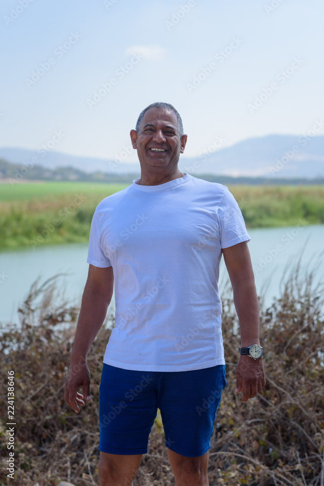 Portrait Of Handsome Senior Man Outdoors. Sporty athletic elderly man on background of sky and lake. Senior standing in nature background.