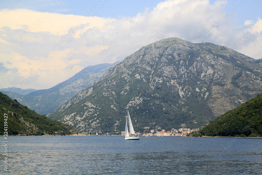 Naklejka premium spectacular views of the boat in the middle of the Bay of Kotor and the city of Perast at the foot of the mountain behind