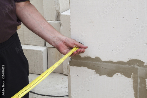 Close up view of the hand holding the measuring tape next to the foam block. Builders measure the width and length of the building under construction.