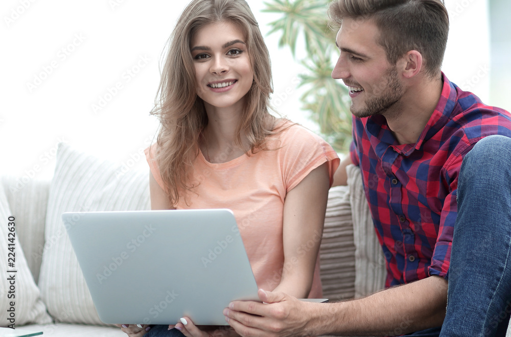 young couple sitting on sofa and looking at pictures on the laptop. young couple sitting on sofa and looking at pictures on the laptop.