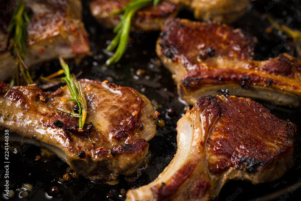 Closeup of Lamb chops frying in a rustic metal pan with rosemary and mixed pepper