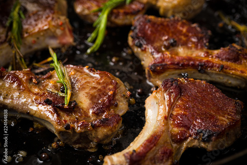 Closeup of Lamb chops frying in a rustic metal pan with rosemary and mixed pepper
