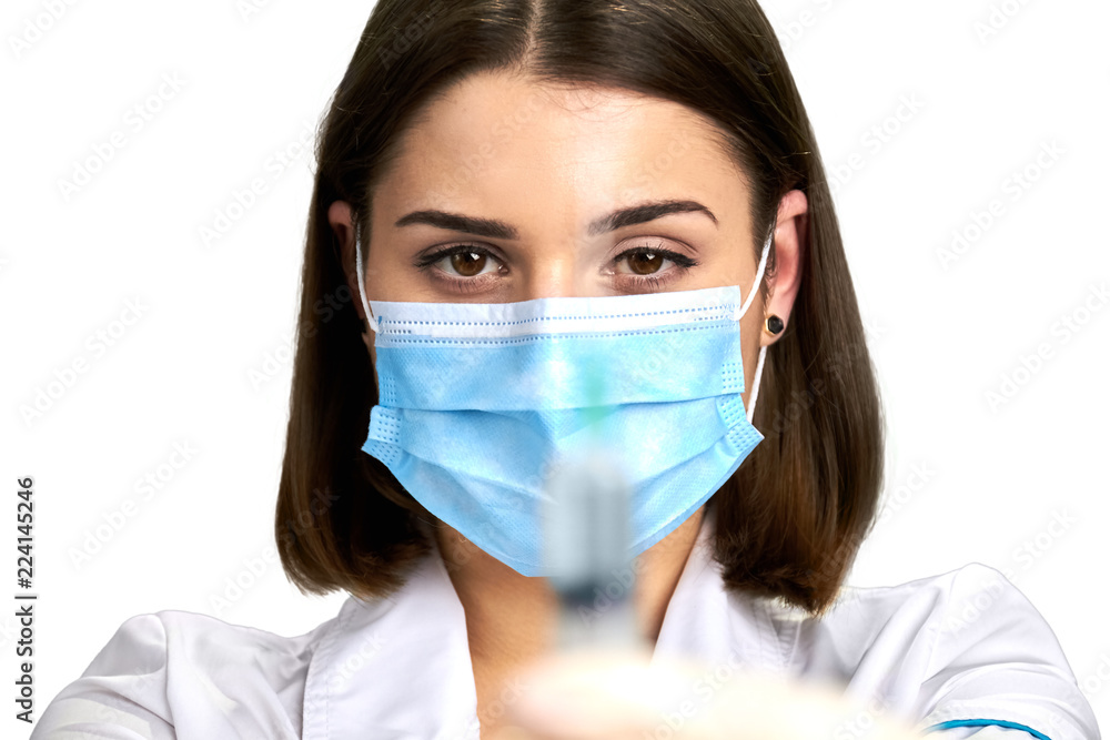 Close up young doctor with injection. Pretty nurse in face mask holding syringe and looking at camera close up. Close up young doctor with injection. Pretty nurse in face mask holding syringe and looking at camera close up.