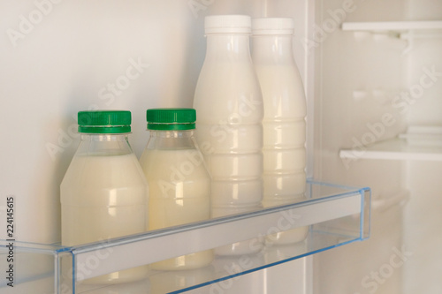 White bottles with green lid of yoghurt on shelf of open empty fridge. Weight loss diet concept. Fermented food.