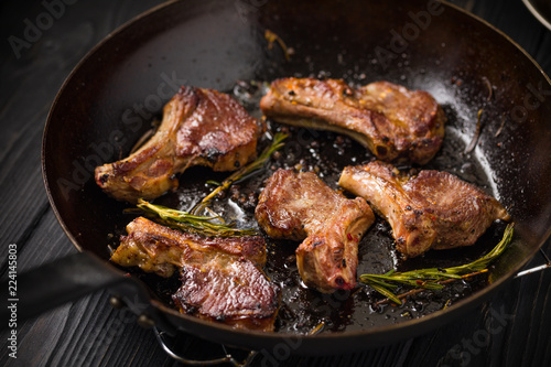 Lamb chops frying in a rustic metal pan with rosemary and mixed pepper