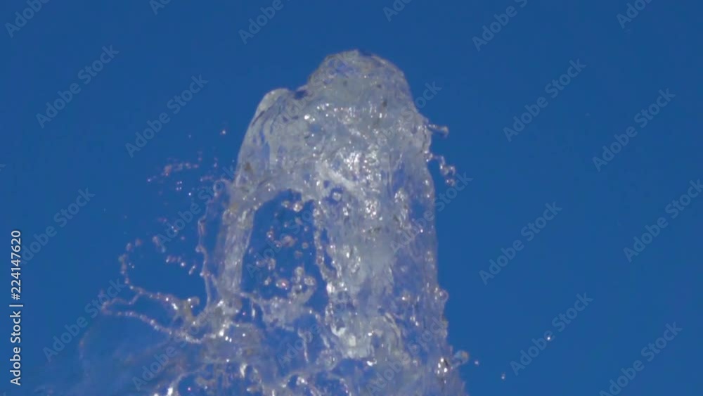 A splash of clear ice water. Closeup of light splashing water in sunny fountain in park in summer on blue sky background. Water flow of fountain fly up in air with many splashes. Slow motion. A splash of clear ice water. Closeup of light splashing water in sunny fountain in park in summer on blue sky background. Water flow of fountain fly up in air with many splashes. Slow motion.