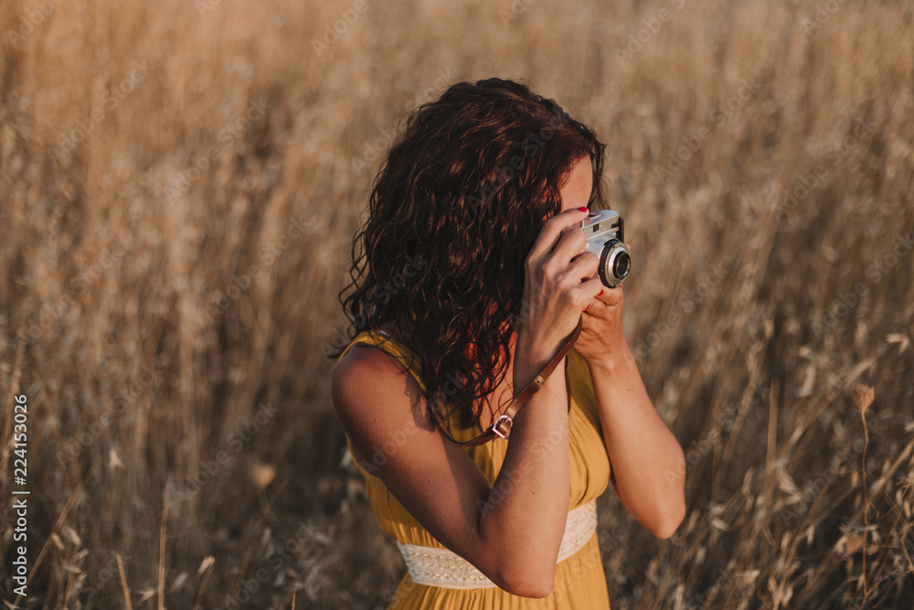Young beautiful woman in yellow dress taking pictures with an old vintage camera. Countryside. Outdoors. Travel concept Young beautiful woman in yellow dress taking pictures with an old vintage camera. Countryside. Outdoors. Travel concept