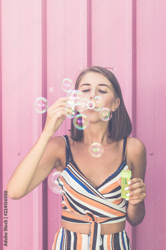 Young hipster female blowing soap balloons over rose wall. Young hipster female blowing soap balloons over rose wall.