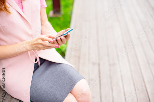 Beautiful young girl sitting on a wooden bench in the open Looking at the mobile phone Women's hands Sunny day green bushes lifestyle Selective focus copy space