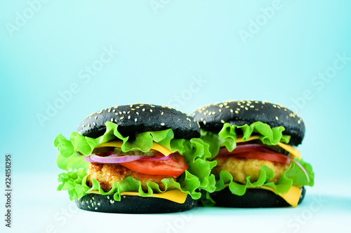 Unhealthy black burgers with beef, cheese, lettuce, onion, tomatoes on blue background. Take away meal. Unhealthy diet concept. Copy space