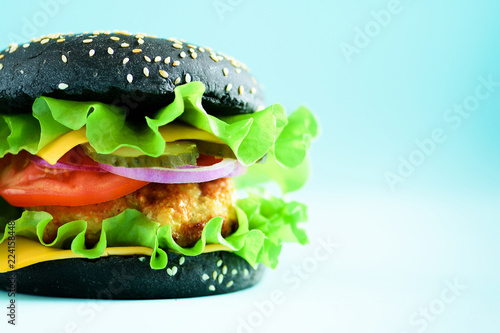Macro view of tasty black burger with beef, cheese, lettuce, onion, tomatoes on blue background. Close up banner. Unhealthy diet concept and copy space