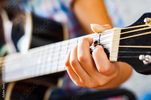 Closeup of young woman hand playing on black acoustic guitar 