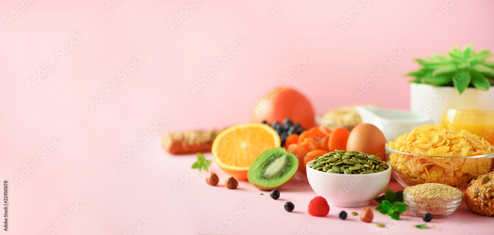 Obraz premium Organic food frame. Banner. Healthy breakfast ingredients. Oat and corn flakes, eggs, nuts, fruits, berries, toast, milk, yogurt, orange, banana, peach on pink background. Top view, copy space