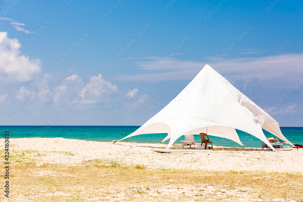 The sun loungers under the big sun shade on the idyllic beach. white tent on the beach.