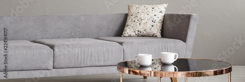 Real photo with close-up of two coffee cups placed on rose gold end table in room interior with grey sofa with lastrico cushion
