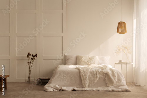 Lamp above white bed with pillows in minimal bedroom interior with plants and stool. Real photo