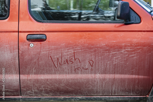 Very dirty red car. The door has text; Wash me!