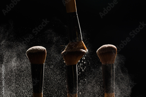Make up, beauty and mineral cosmetics concept - Brush brushing away a powder from another brush on dark background
