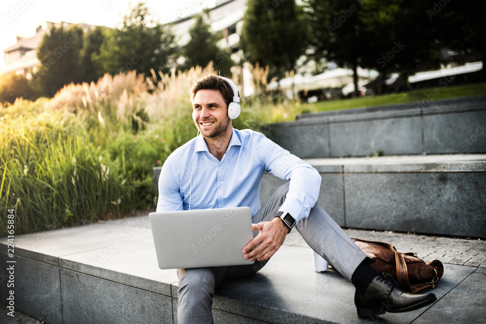 A businessman with headphones sitting outdoors on stairs, listening to music. A businessman with headphones sitting outdoors on stairs, listening to music.