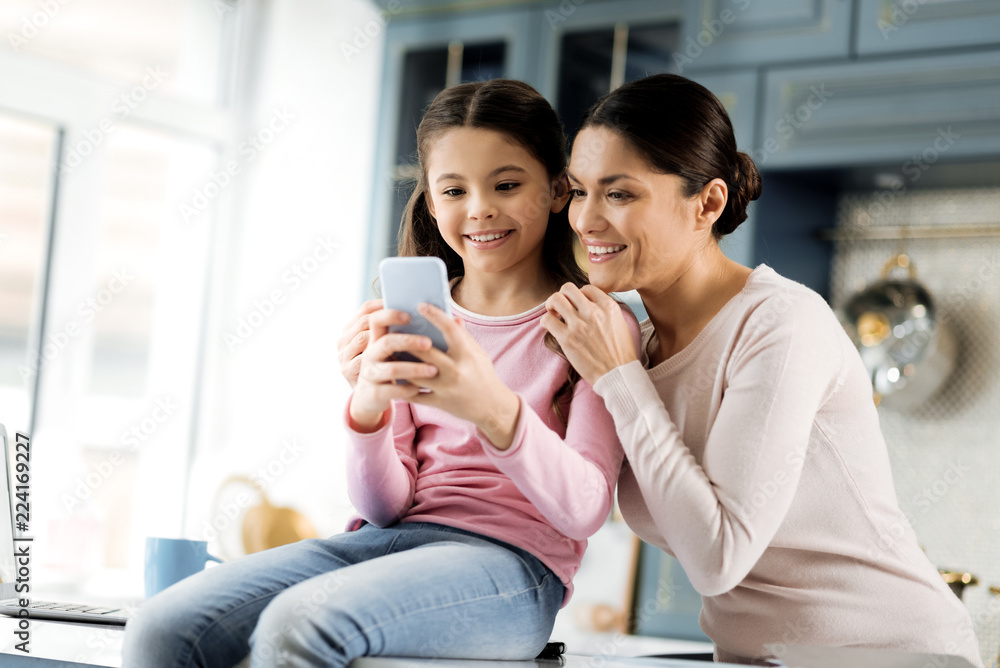 Cute picture. Low angle of glad energetic girl utilizing phone and woman laughing Cute picture. Low angle of glad energetic girl utilizing phone and woman laughing