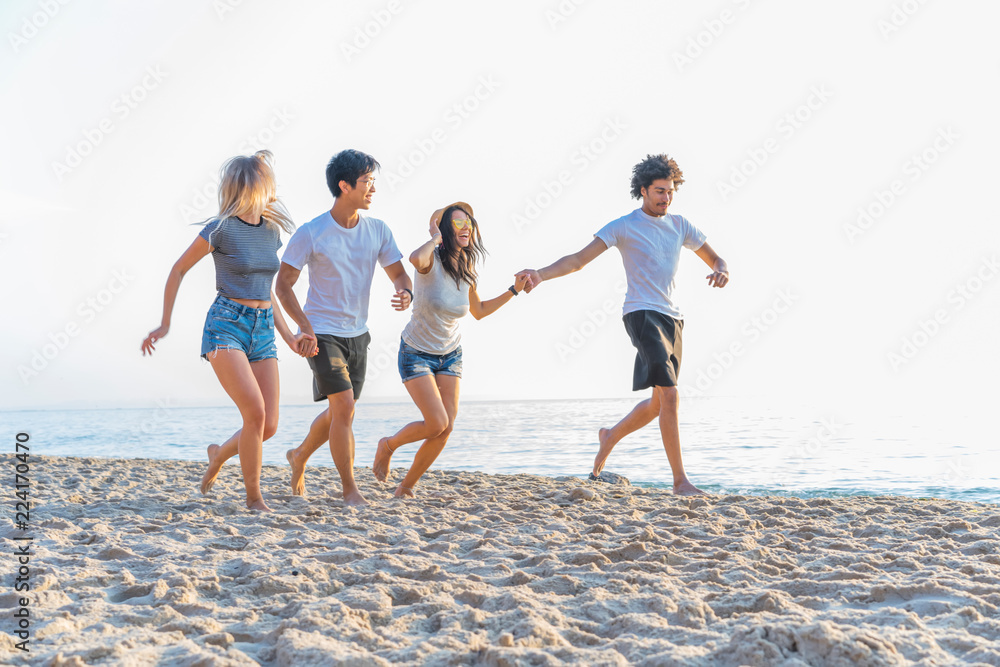 Group of friends having fun running down the beach at sunset.
