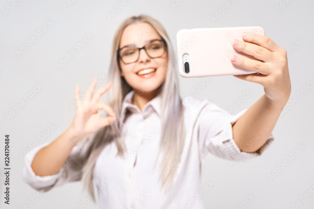 Portrait of a smiling cute woman in glasses making selfie photo on smartphone isolated on a white background. Portrait of a smiling cute woman in glasses making selfie photo on smartphone isolated on a white background.