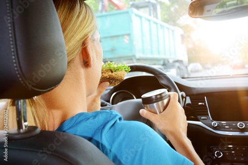 Canvas Print Woman as a driver eats and drinks during the car ride and is therefore careless