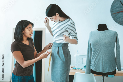 Professional model. Serious dressmaker standing in semi position while taking measurements of her visitor photo