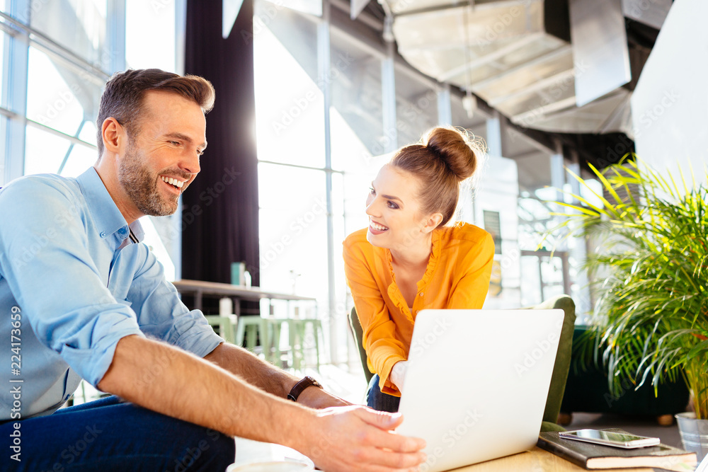 Two cheerful business partners chatting during meeting in restaurant and looking at laptop Two cheerful business partners chatting during meeting in restaurant and looking at laptop