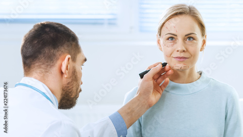 Over the Shoulder Shot of a Plastic / Cosmetic Surgeon Draws Lines on a Face of a Beautiful Female model for the Facelift Operation.