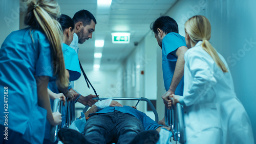 Emergency Department: Doctors, Nurses and Surgeons Move Seriously Injured Patient Lying on a Stretcher Through Hospital Corridors. Medical Staff in a Hurry Move Patient into Operating Theater. photo
